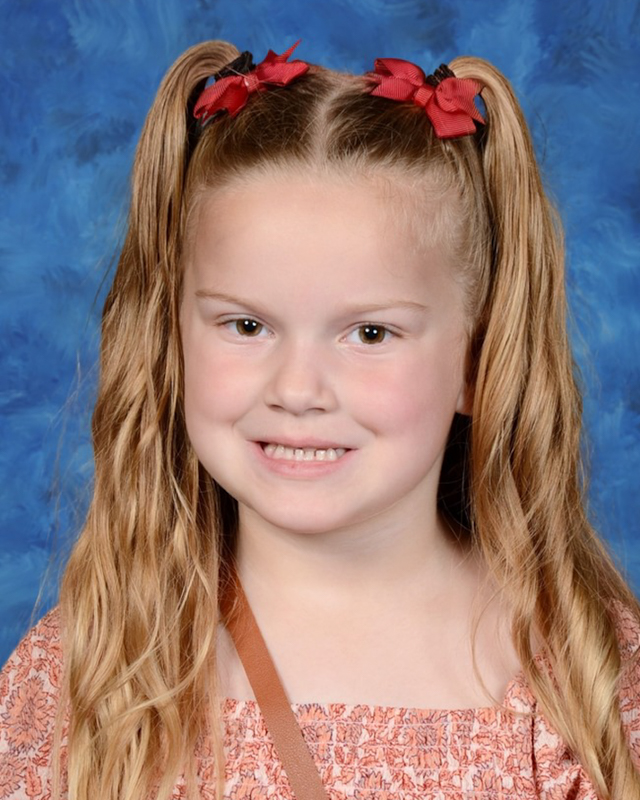 young girl with long blonde hair gives a toothy smile